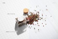 Round spice jar with editable label mockup, jar tipped over with mixed peppercorns spilled on white wood surface.