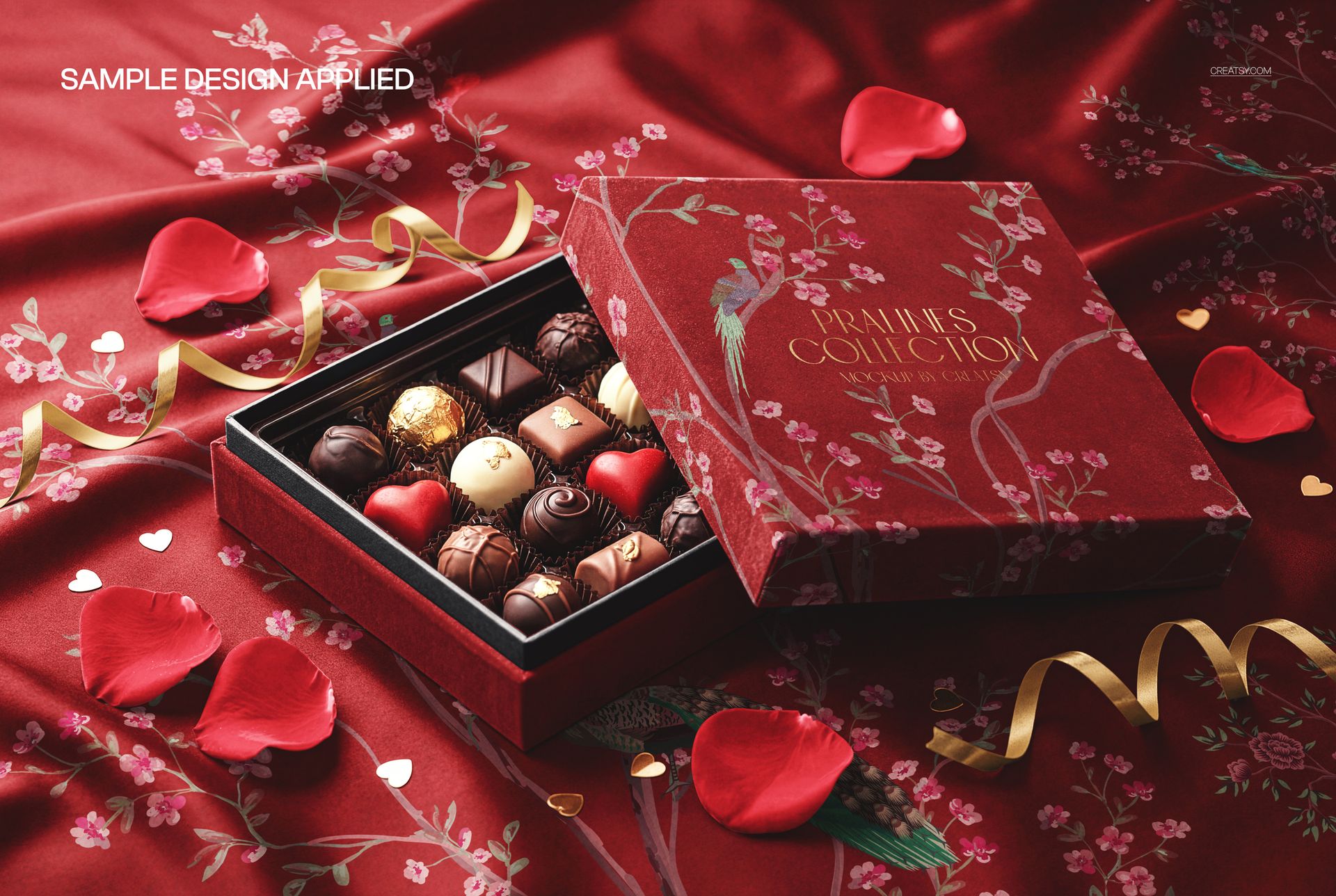 PSD mockup showing a square praline box and chocolates on floral red velvet, rose petals and ribbon accents, angled perspective.