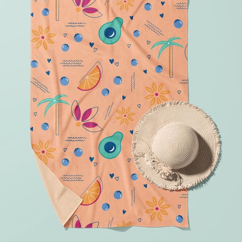 Beach towel mockup featuring a pastel towel with colorful fruit, palm tree, and sun illustrations, styled with a straw hat on a light blue background.