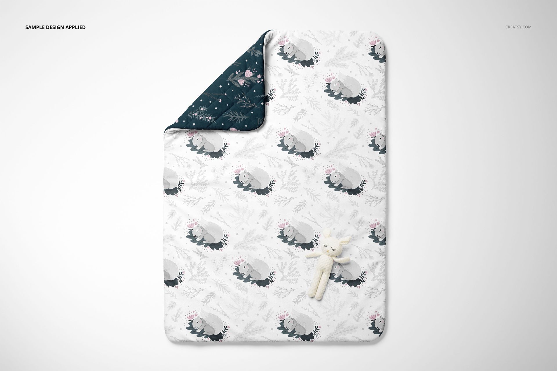 Top view of a double-sided baby bedding mockup set with a patterned quilt and small plush toy on a plain surface.