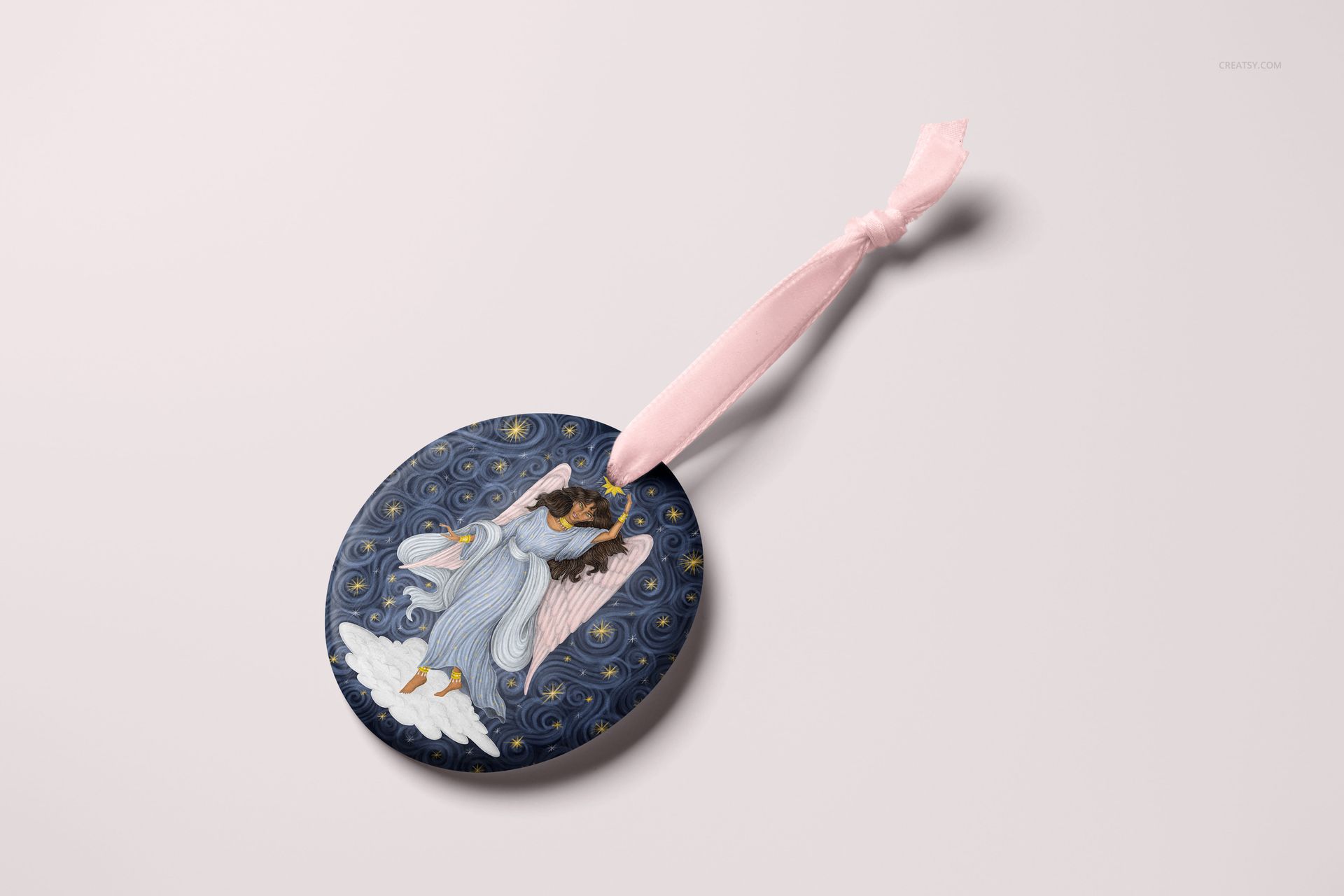 Oval-shaped Christmas ornament mockup featuring an angel illustration on a dark blue background with swirling patterns.