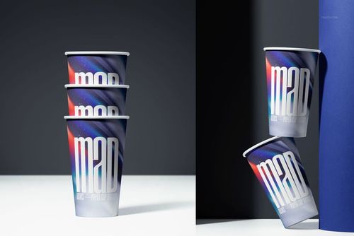 Stacked paper cups with a bold, colorful abstract design and large text, shown on a white surface and dark background.
