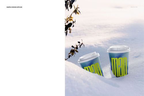 PSD mockup featuring a pair of drinkware paper cups with colorful patterns, resting in fresh snow near leafy branches.