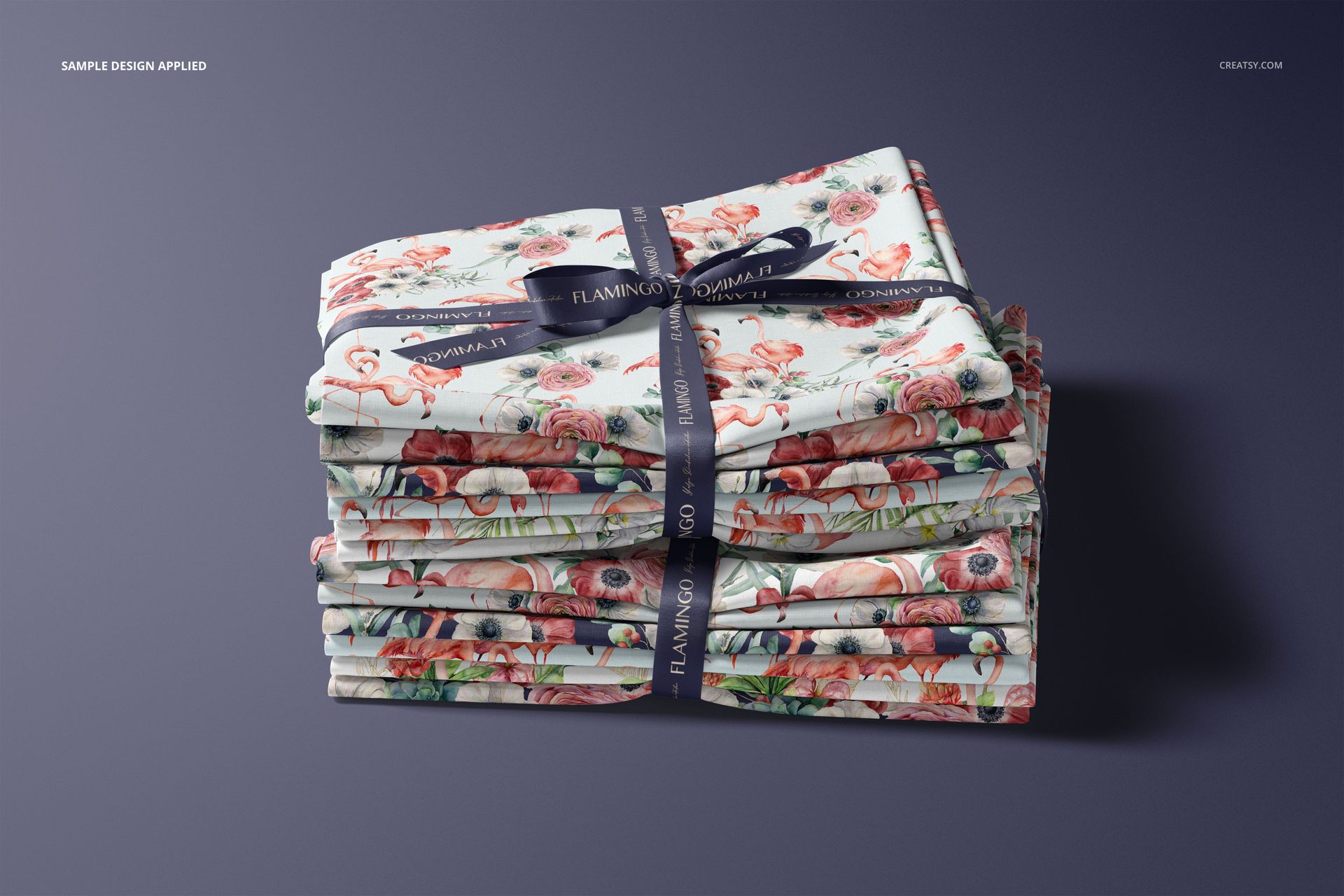 PSD mockup of stacked textiles with colorful flamingo and botanical prints, viewed from the front on a dark background.