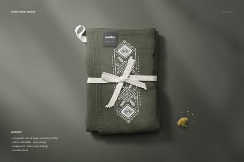 Folded kitchen towel mockup in dark green color with white geometric pattern, tied with a ribbon, top view on gray surface.
