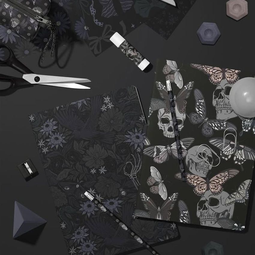 Stationery mockup featuring two classic A4 notebooks with dark floral and skull patterns, surrounded by pencils, scissors, and geometric props on a black surface.