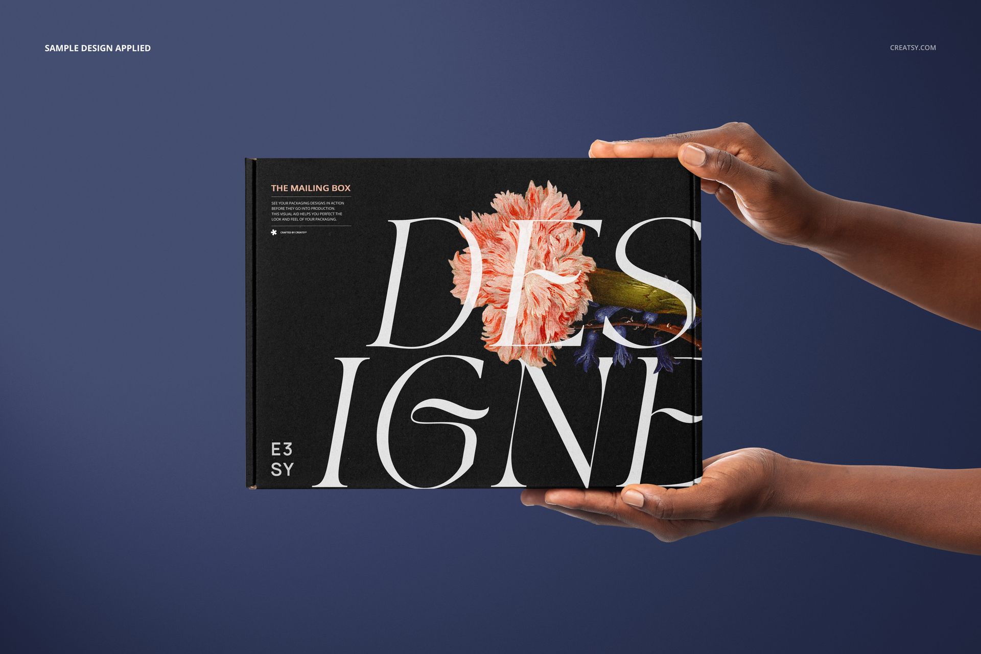 Mailing box mockup featuring a black surface with large white letters and a pink flower, presented in hands on blue.