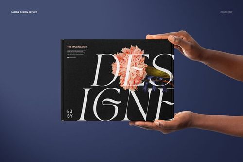 Mailing box mockup featuring a black surface with large white letters and a pink flower, presented in hands on blue.