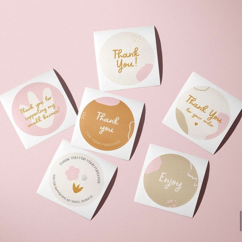 Sticker mockup featuring six square sticker sheets with round stickers, each showing pastel colors and handwritten text on a pink background.