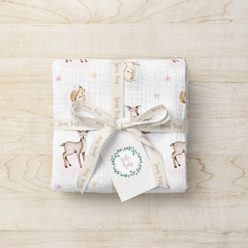 Crinkle muslin swaddle blanket mockup featuring a folded white blanket with deer and star illustrations, tied with a printed ribbon.