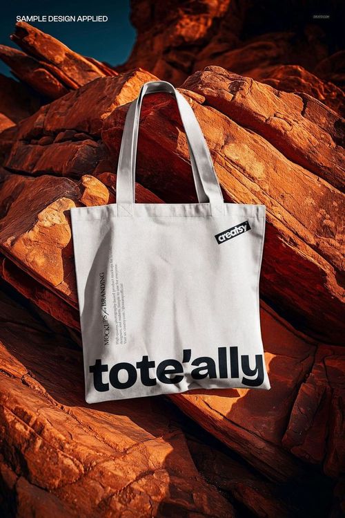 White canvas tote bag with black text design displayed on rugged orange rocks, front view mockup scene.