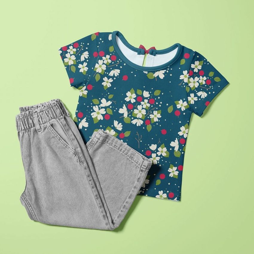 Kids t-shirt and jeans mockup featuring a blue floral shirt with white and pink flowers, paired with light gray pants on a green background.