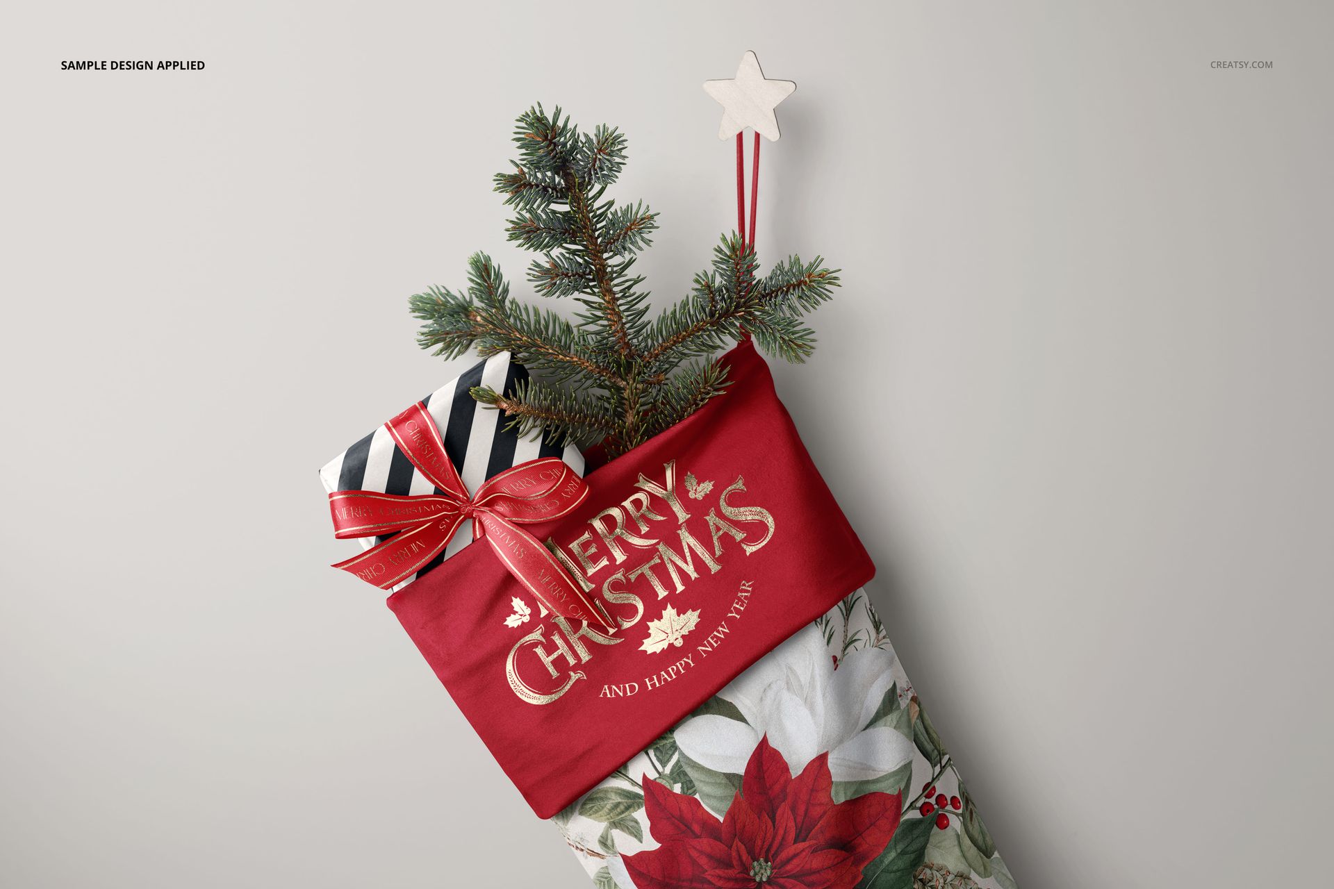 Christmas stocking mockup with red cuff, floral pattern, spruce branch, wrapped gift, and star-shaped hanger, top view.