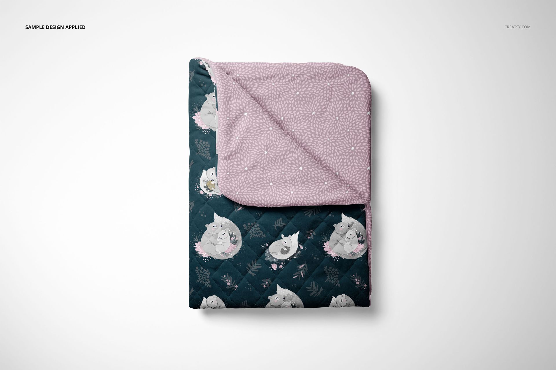 Folded baby quilt mockup featuring a whimsical animal print on one side and a soft pink dotted pattern on the other.
