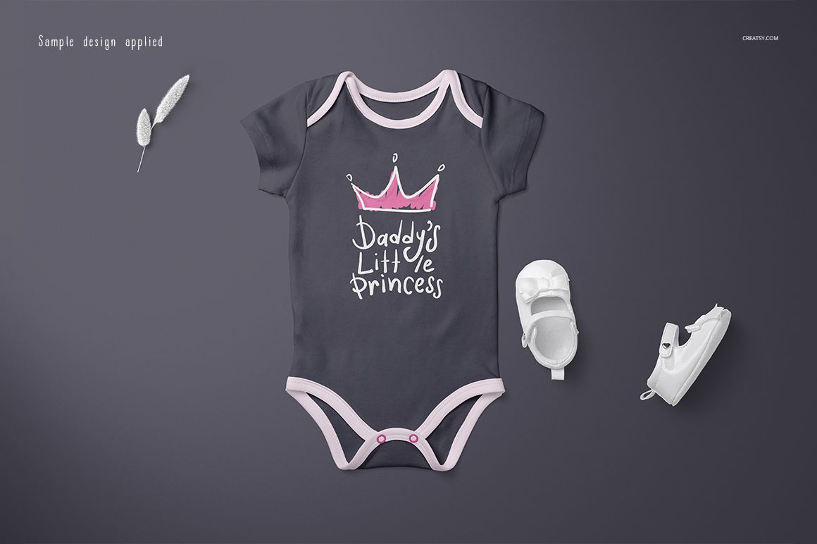 PSD mockup of a short-sleeve baby onesie in dark gray with pink edges, shown with a crown design and shoes nearby.