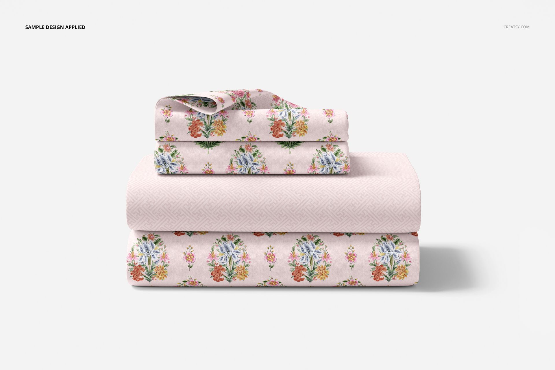 Front view of a bedding set mockup with folded sheets and pillowcases featuring colorful floral designs on pale pink.