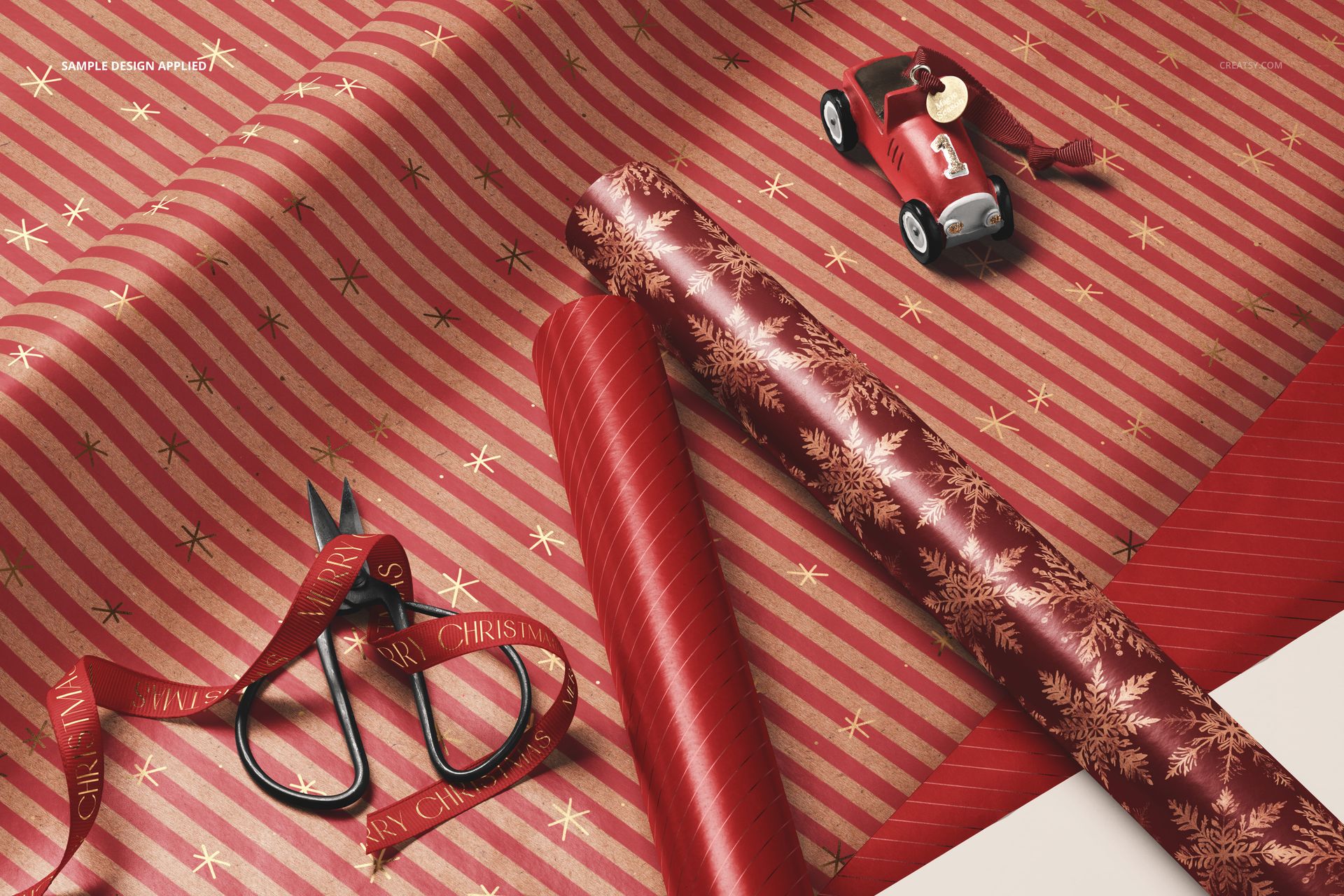 Close-up of Christmas gift wrapping paper mockup with red and gold striped and snowflake patterns, scissors, and toy car.