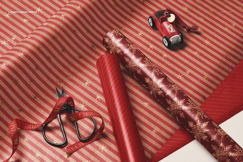 Close-up of Christmas gift wrapping paper mockup with red and gold striped and snowflake patterns, scissors, and toy car.