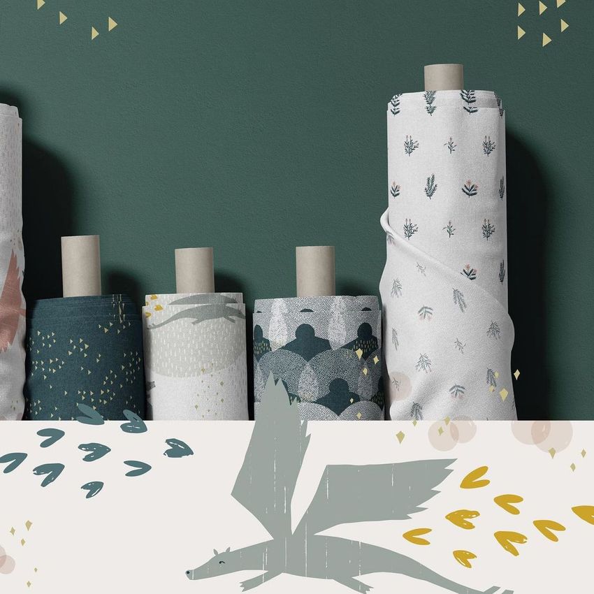 Fabric rolls mockup featuring several upright rolls with various abstract and nature-inspired patterns against a green wall.