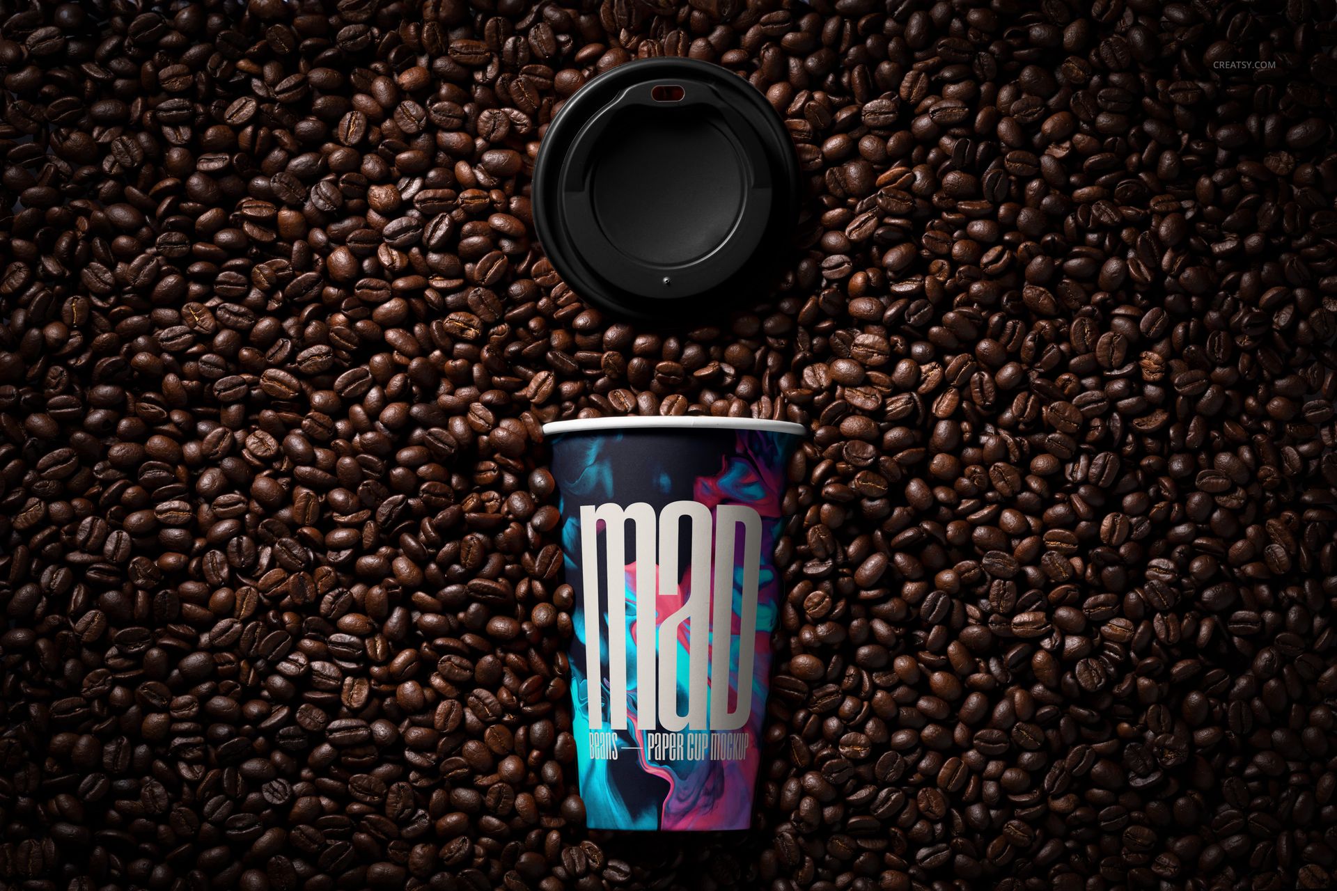 PSD mockup showing a paper cup with bold graphics lying on a bed of coffee beans, lid positioned at the top.