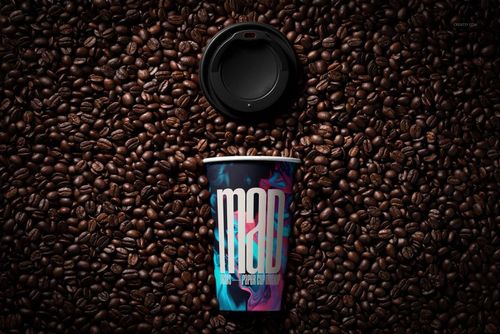 PSD mockup showing a paper cup with bold graphics lying on a bed of coffee beans, lid positioned at the top.