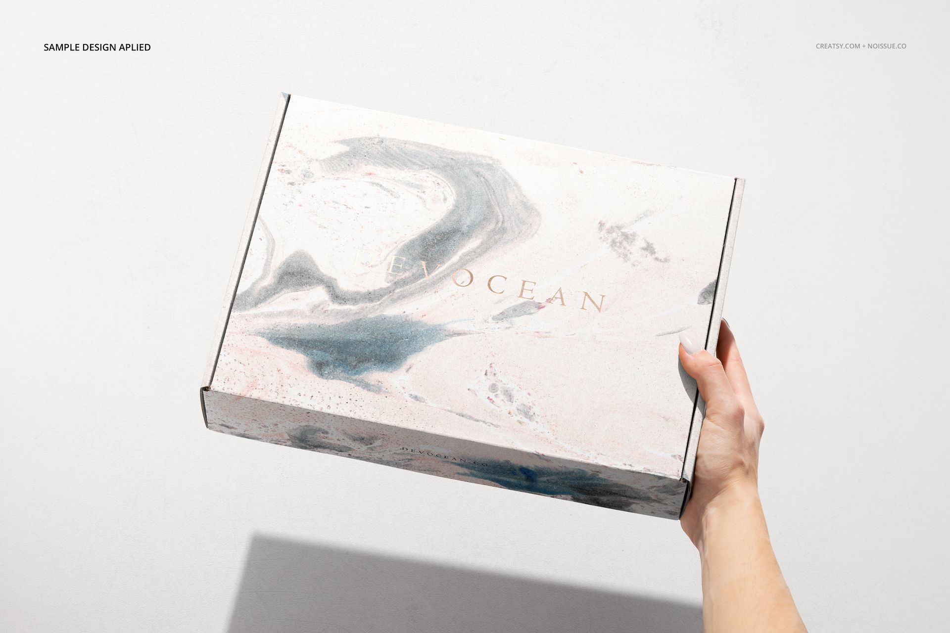 Front view of a packaging box mockup featuring a soft marbled design and subtle branding, held against a plain wall.