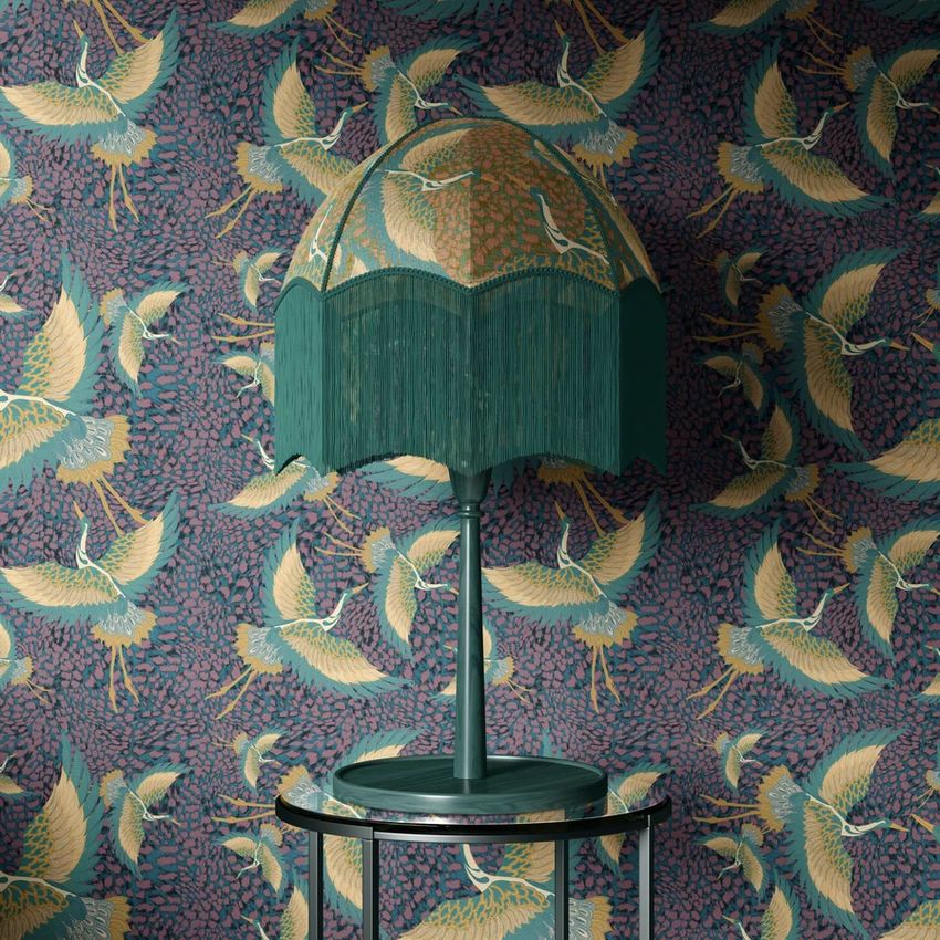 Vintage velvet fringe table lamp mockup on a round glass table, set against a patterned wallpaper with crane illustrations.