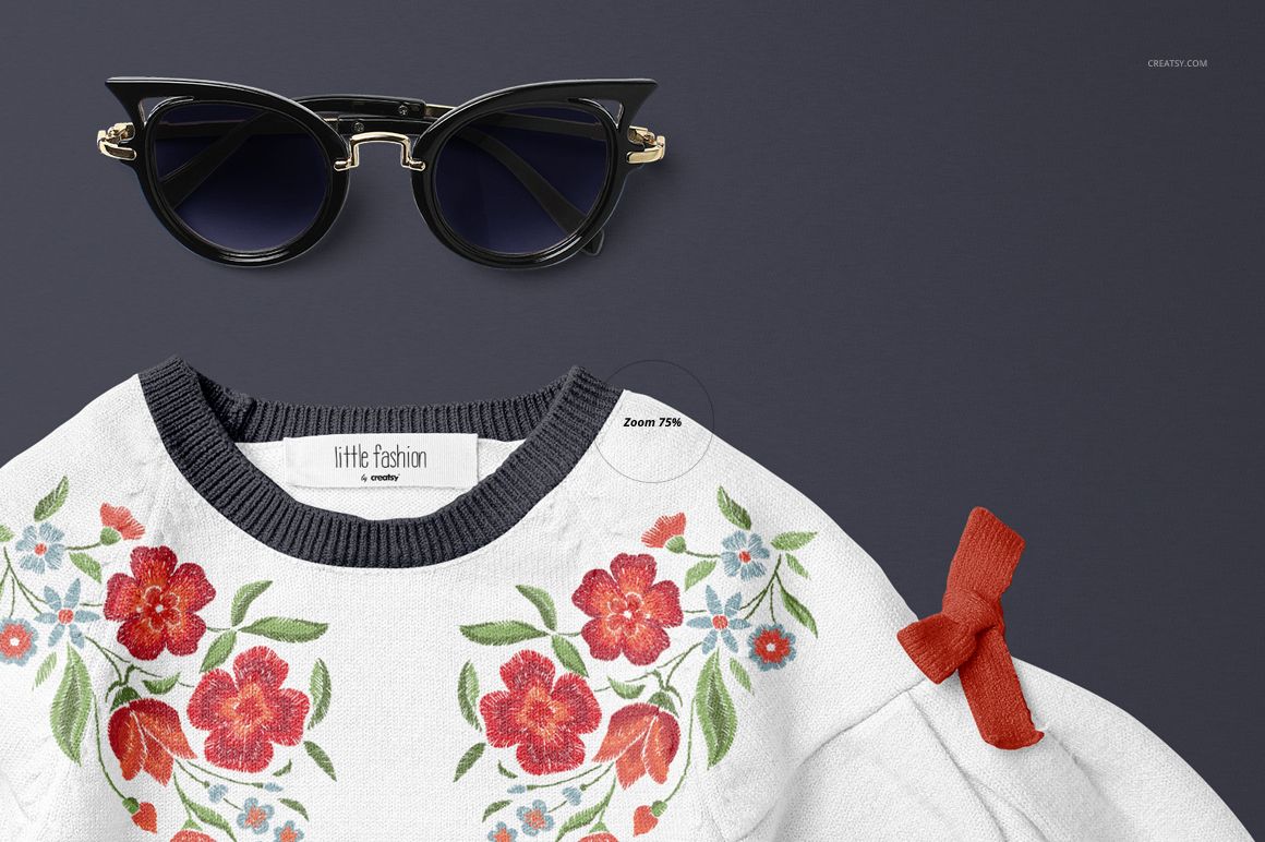 Close-up of a white baby sweater mockup with colorful floral embroidery and a red bow accent on the sleeve.