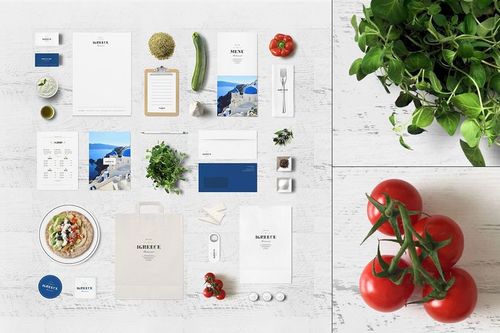 Greek restaurant branding mockup with stationery, food items, herbs, and vegetables arranged on a white wooden surface.