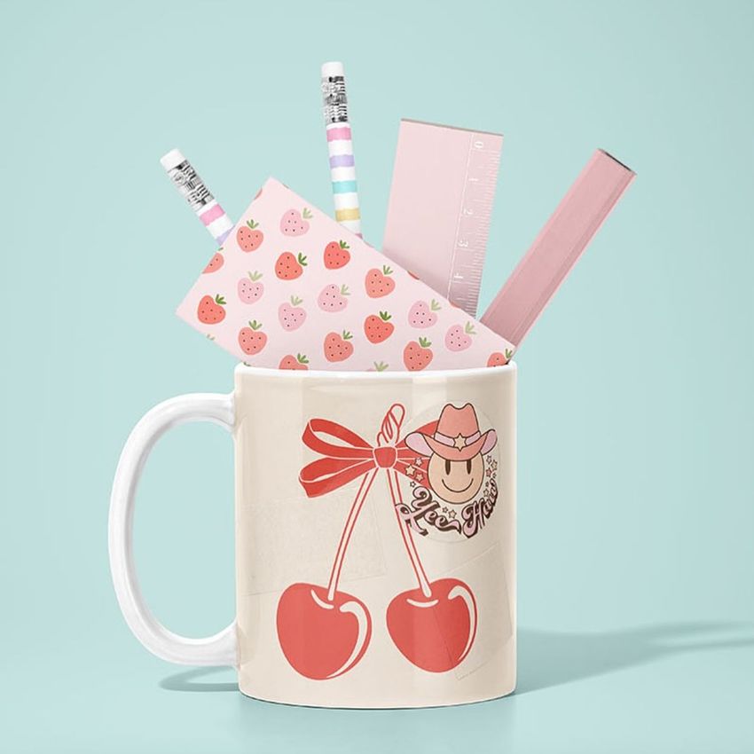 Mug mockup with a cherry-themed illustration, holding striped pencils, a pink ruler, and a patterned notecard on a pastel background.