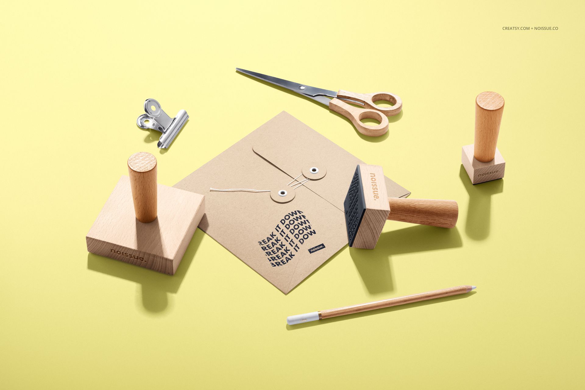 Set of wooden stamps, envelope, scissors, and pencil displayed on a yellow background in a stationery mockup.
