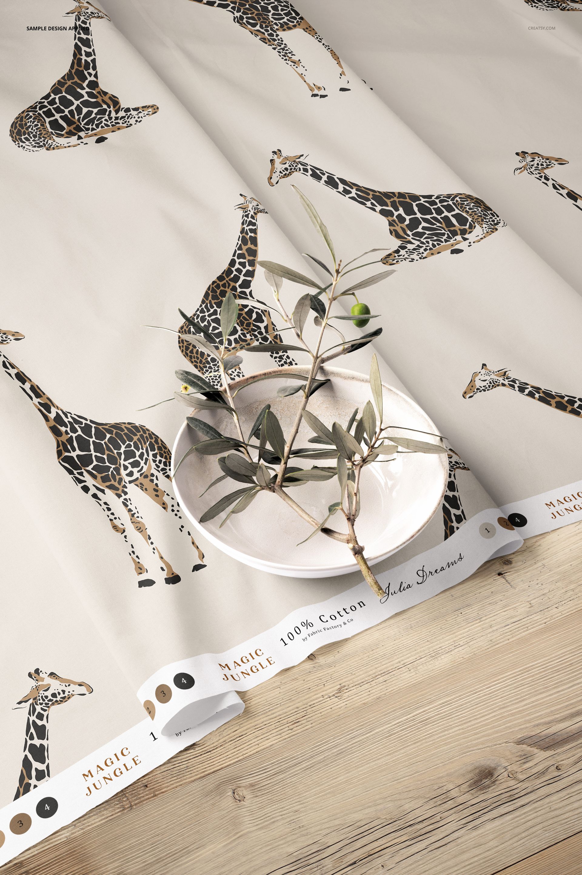 Cotton fabric mockup featuring a giraffe pattern, displayed with a white bowl and olive branch on a wooden surface.
