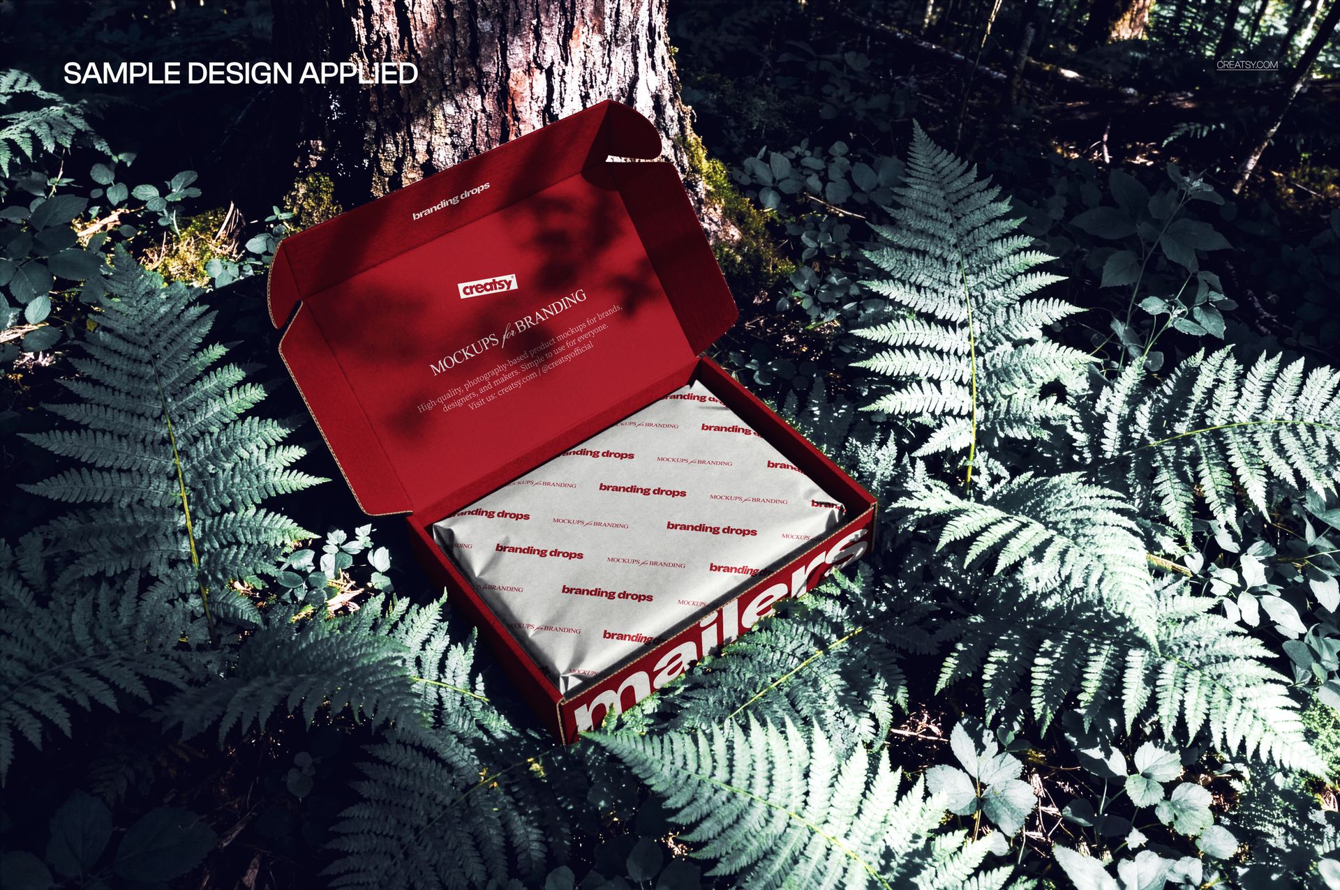 PSD mockup of an open mailing box with printed tissue paper, surrounded by ferns and tree trunks in a forest setting.