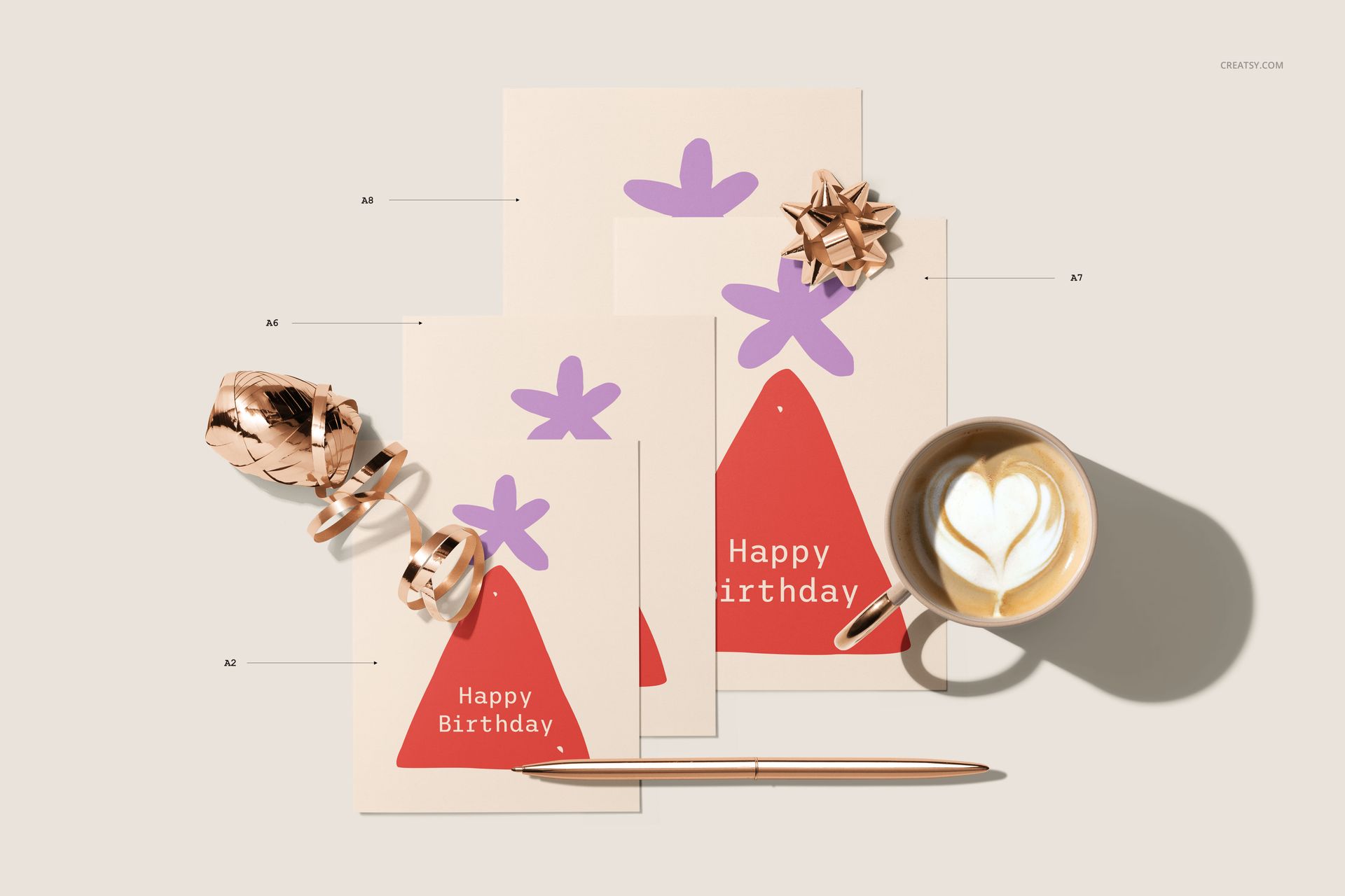 Four greeting cards of varying sizes with matching envelopes, displayed on a beige surface with a pen, bow, and coffee cup.