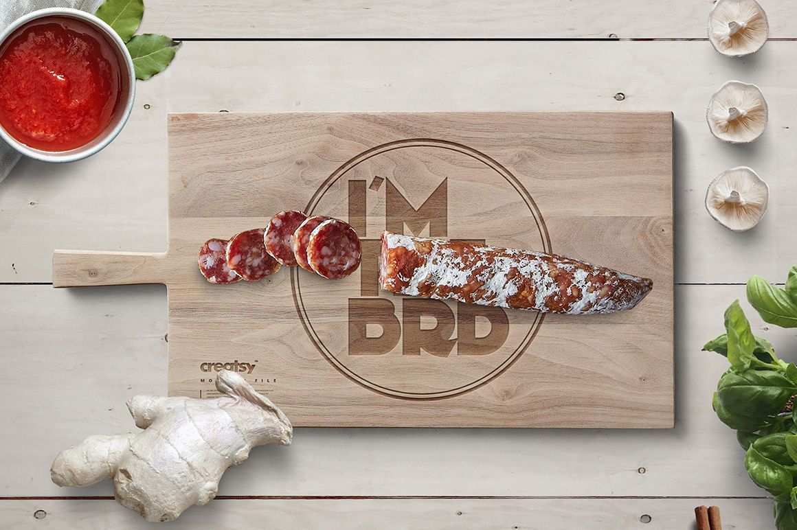 Rectangular engraved wooden board mockup with sliced sausage, knife, and vegetables on a light wood table.