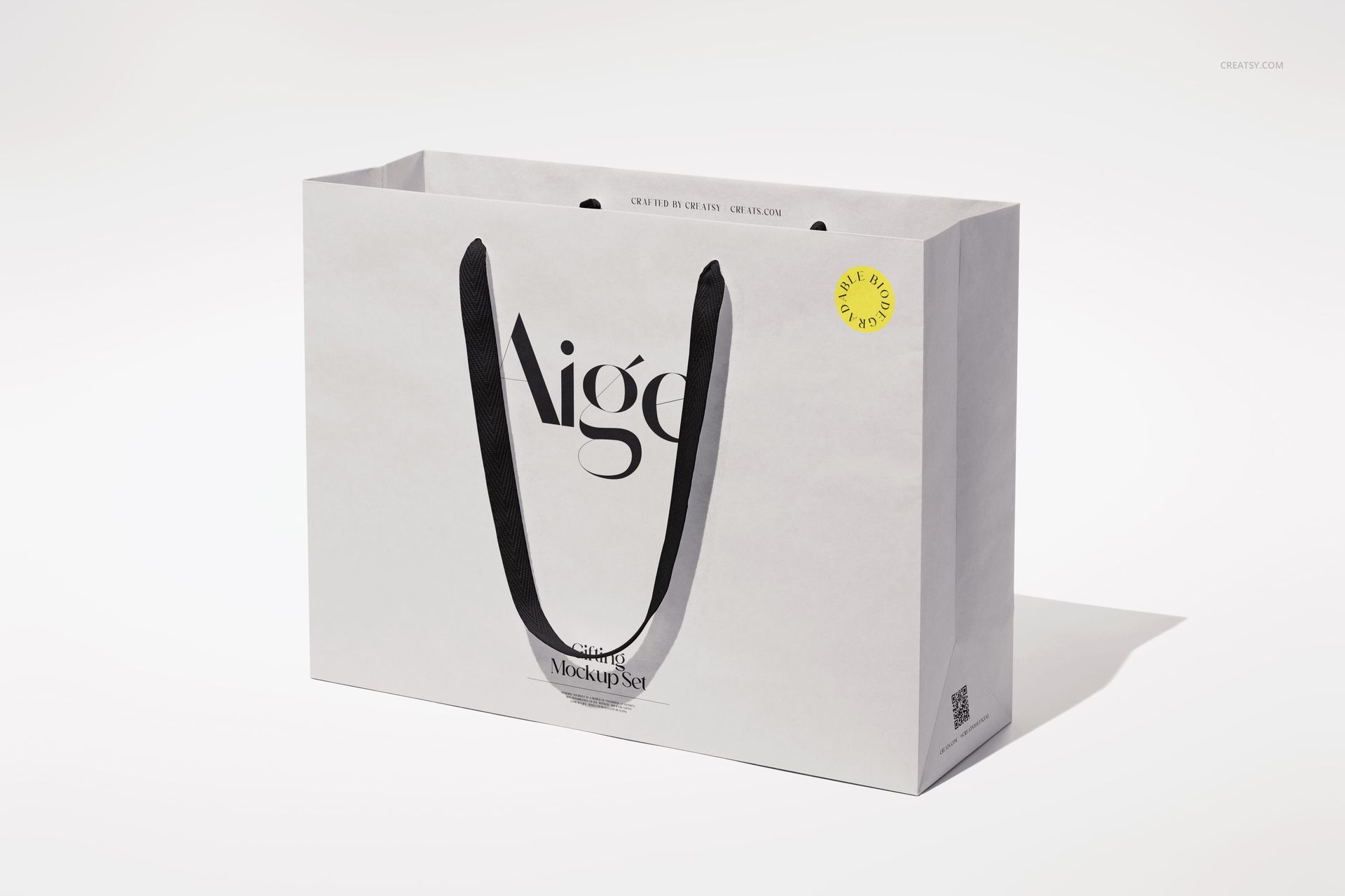 White paper gift bag mockup featuring black ribbon handles, minimalist design, and a soft shadow on a plain surface.