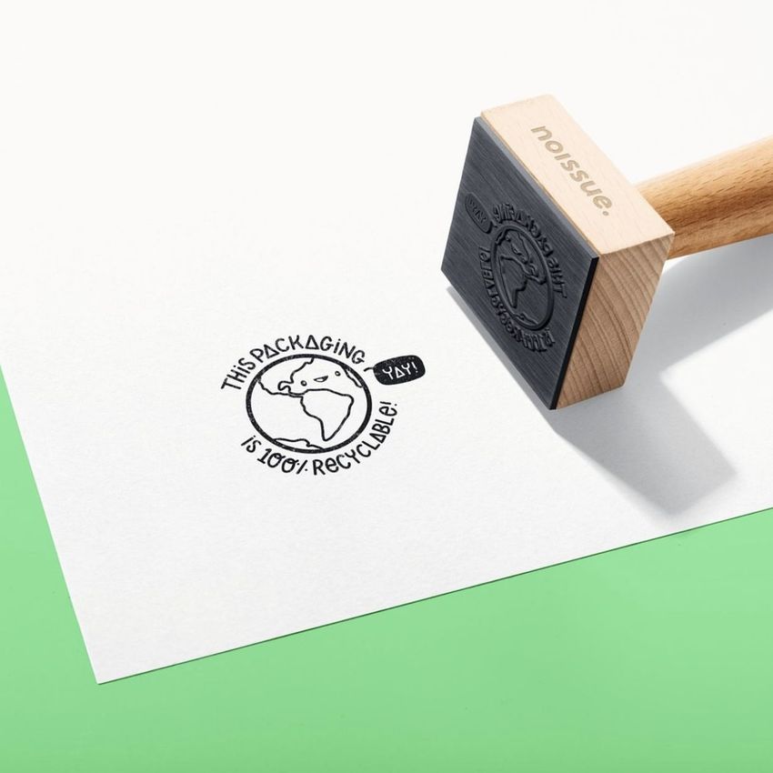 Wooden stamp mockup set on a white sheet of paper with a stamped circular eco-friendly design and green background.