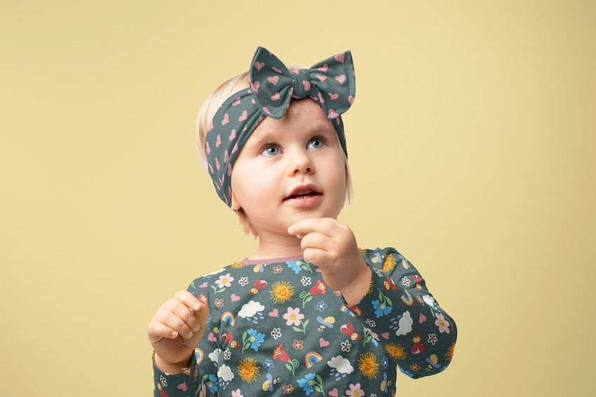 Child wearing a colorful bow tie style headband mockup with matching patterned shirt, standing against a plain beige background.