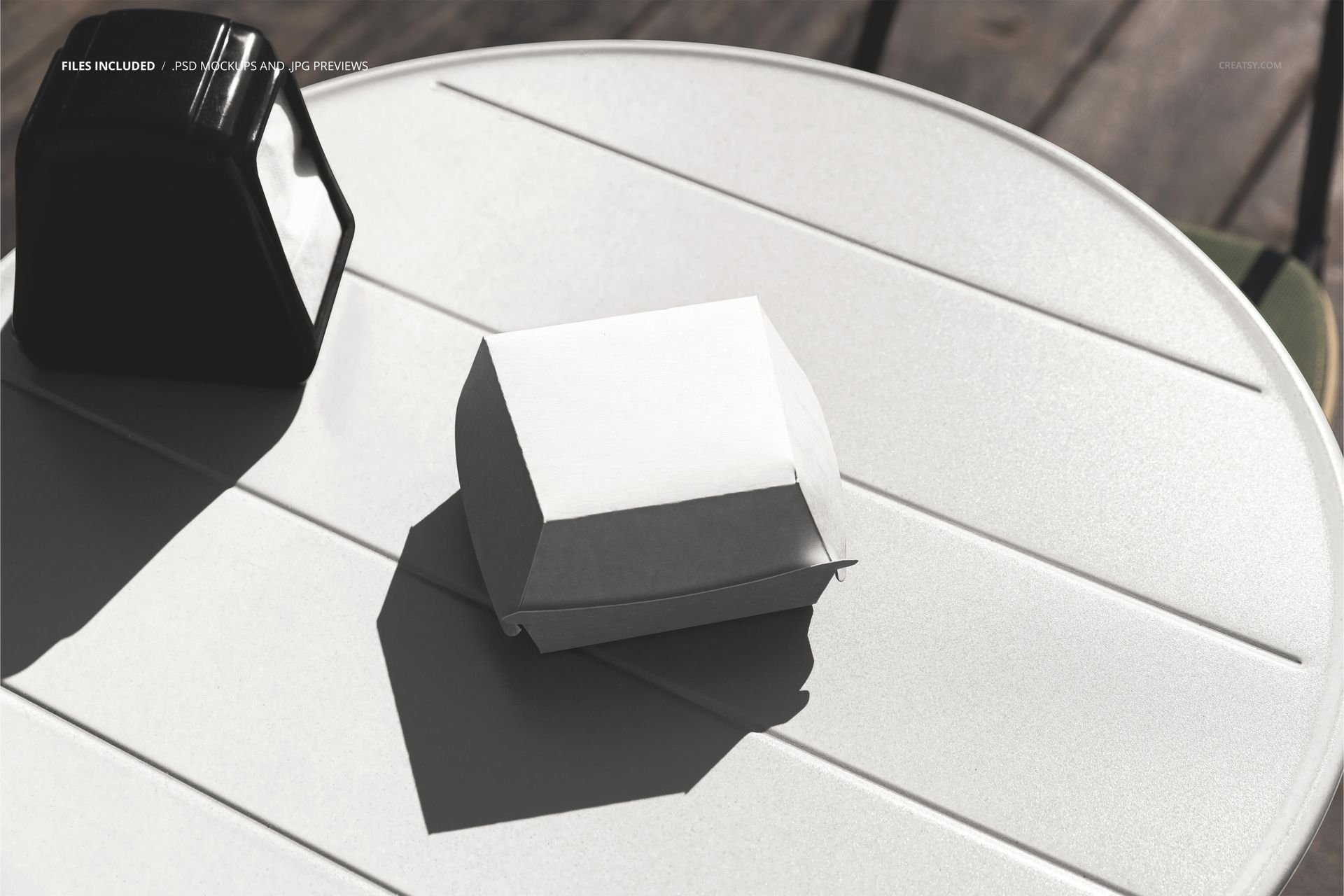 Round outdoor table with white napkins holder and closed burger box mockup in bright sunlight, top view.