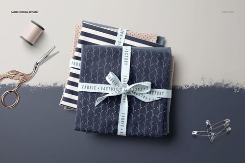 Top view of a fabric stack mockup featuring folded textiles in navy and blush tones, with ribbon and sewing tools nearby.