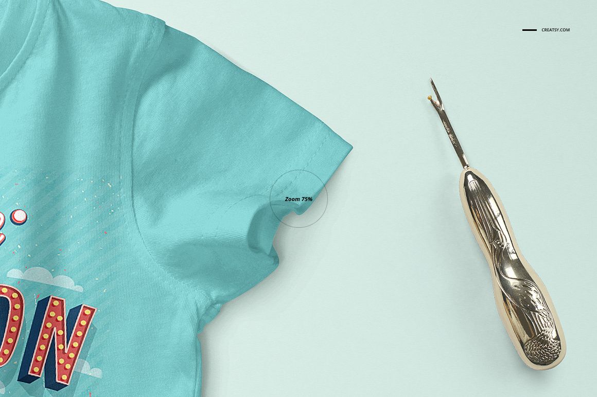 Close-up front view of a light blue baby T-shirt mockup with colorful print details, shown next to a metallic seam ripper on a pale background.