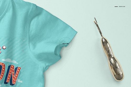 Close-up front view of a light blue baby T-shirt mockup with colorful print details, shown next to a metallic seam ripper on a pale background.
