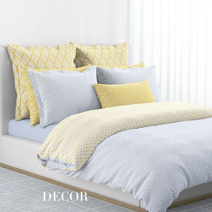 Bedding mockup showing a neatly made bed with geometric patterned pillows and duvet in yellow and light gray tones.