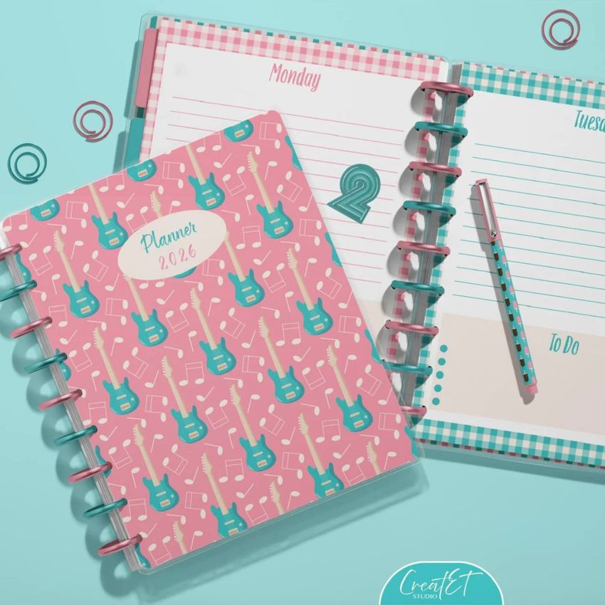 Top view of two spiral planners on a light blue surface, one closed with a pink guitar pattern cover and one open showing lined pages.