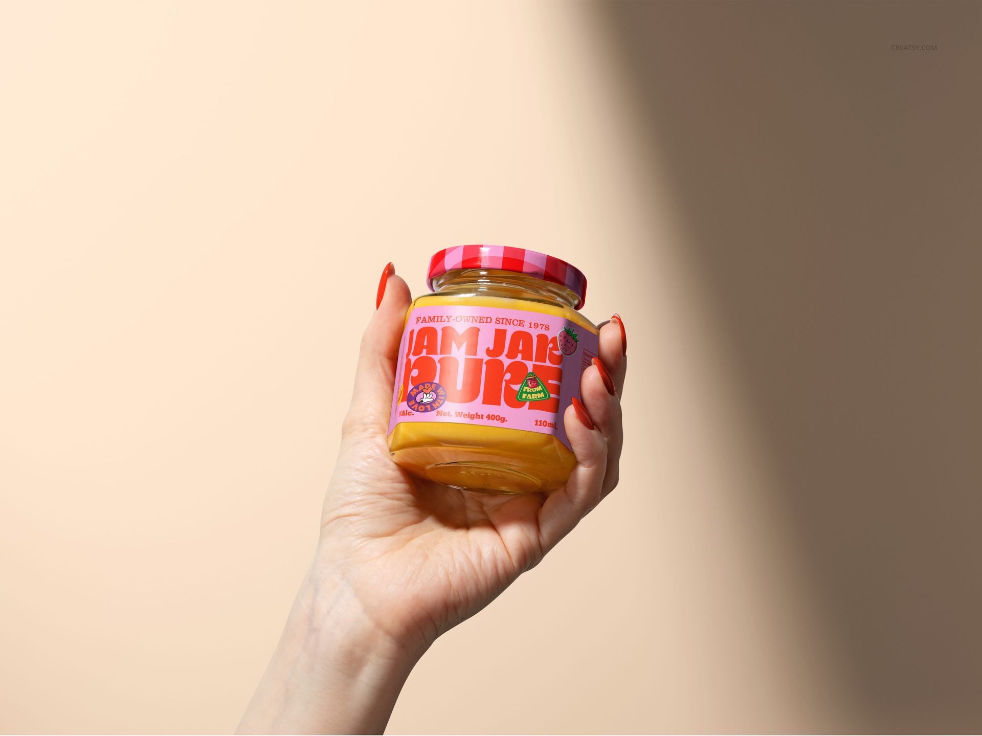 Jam jar mockup shown in a hand, filled with yellow jam, pink patterned lid, and bold text label, studio-lit scene.