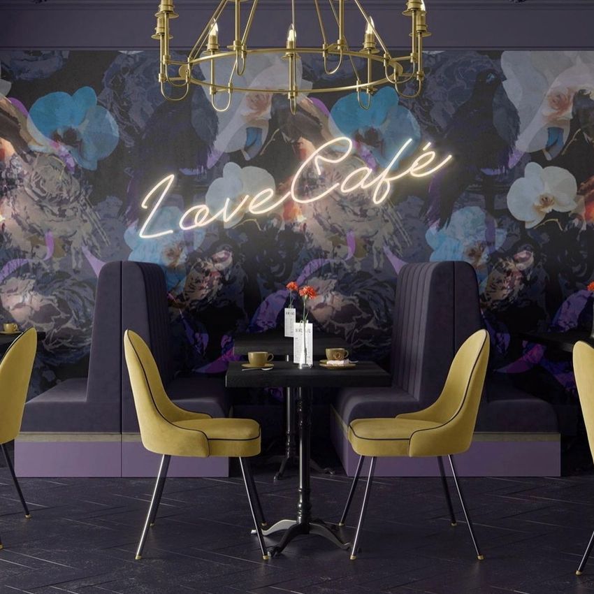 Cafe interior wallpaper mockup showing a dark floral mural with neon-style 'Love Café' text, yellow chairs, and a chandelier.