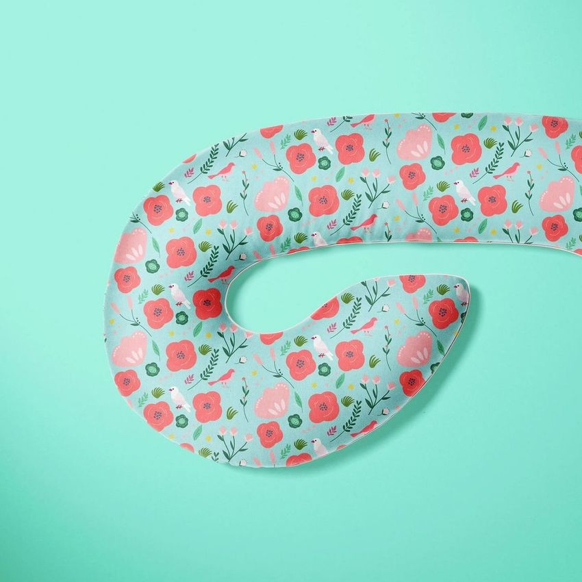 Pregnancy pillow mockup featuring a curved pillow with a red and pink floral pattern on a light blue background.
