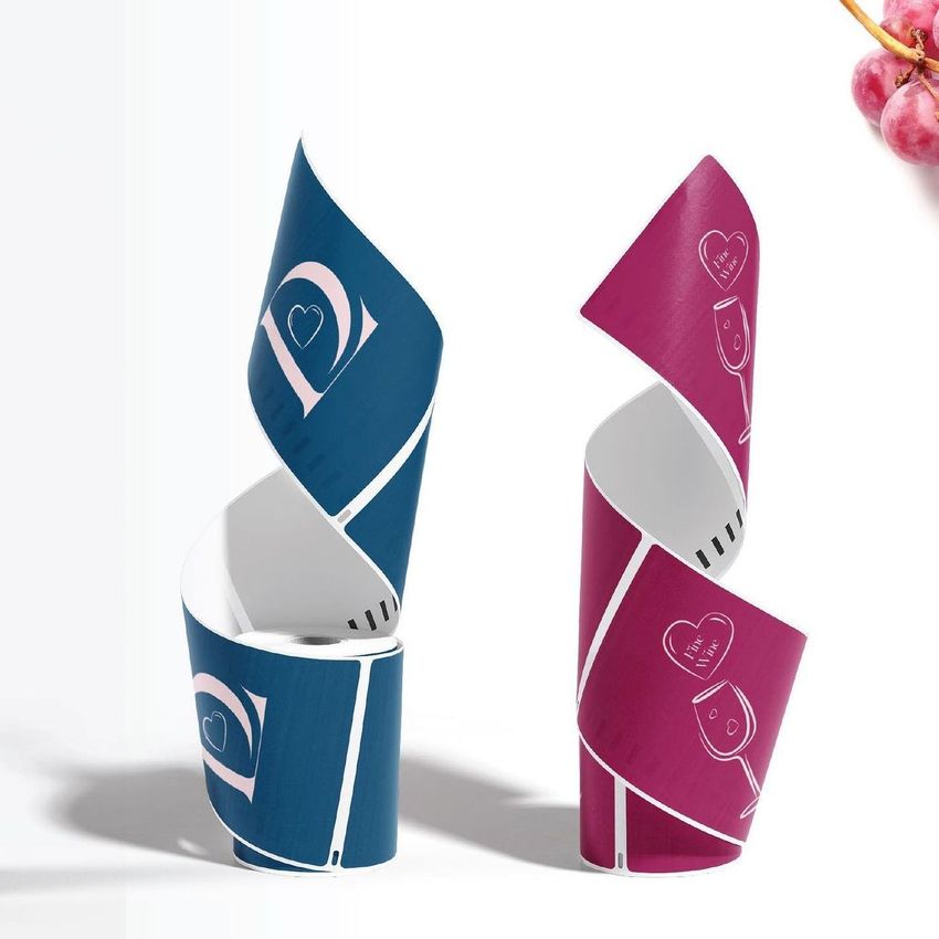 Two spiral-shaped shipping label mockups, one blue and one magenta, stand upright on a white surface with a grape cluster in the corner.