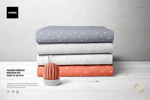 Front view of a fabric stack mockup featuring three folded textiles in muted tones and delicate designs, with a pin cushion nearby.