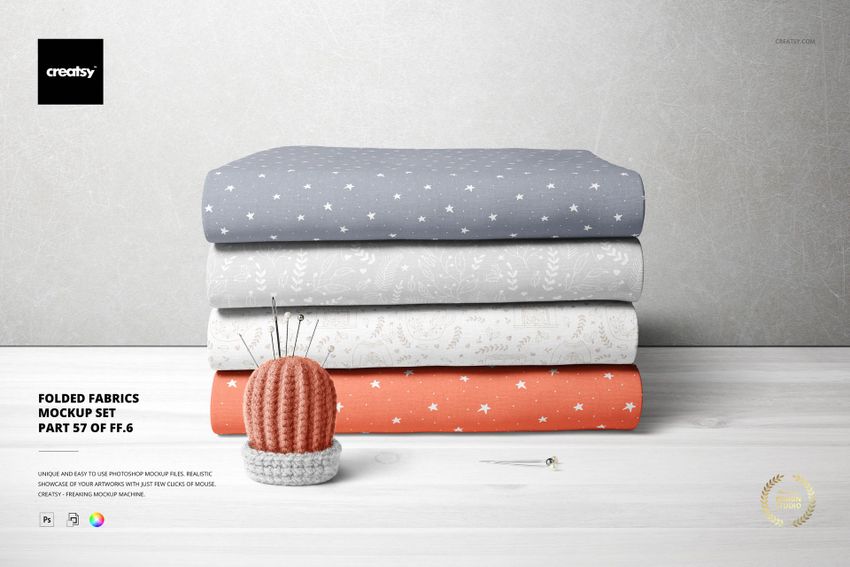 Front view of a fabric stack mockup featuring three folded textiles in muted tones and delicate designs, with a pin cushion nearby.